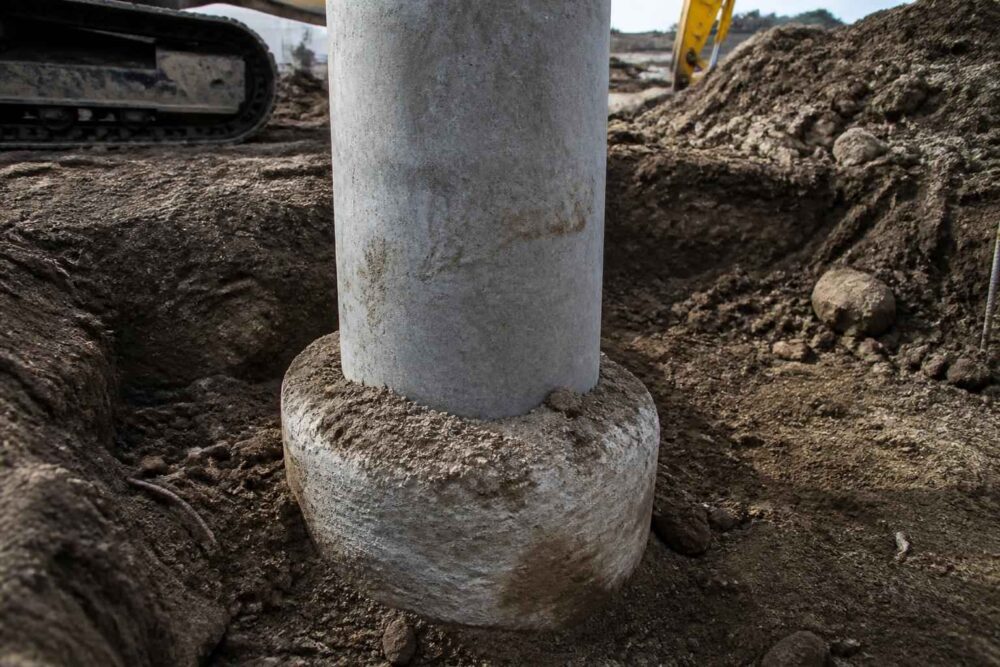 Betonowy słup osadzony w okrągłej podstawie podczas prac ziemnych na placu budowy