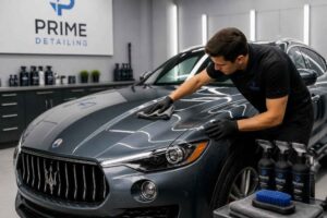 Pracownik studia detailingowego poleruje maskę ciemnego Maserati w profesjonalnym garażu